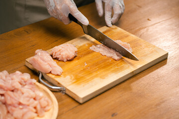 Asian man's hands cutting meat on a wooden cutting board in the kitchen, preparing to cook.