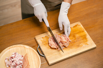 Asian man's hands cutting meat on a wooden cutting board in the kitchen, preparing to cook.