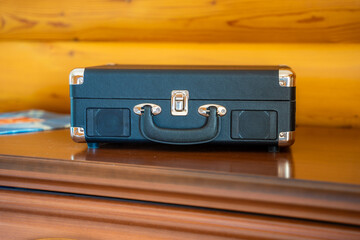 Closed vintage-style record player in suitcase design on wooden table. Retro audio equipment ready...