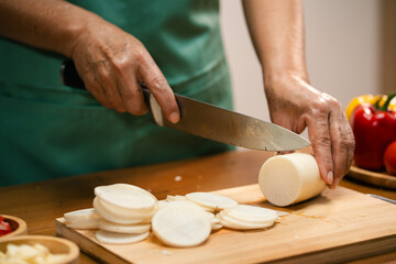 Hands slicing Radish on a wooden board in the kitchen, preparing to cook.