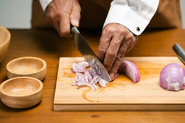 Close up of hands slicing onion on cutting board in kitchen.