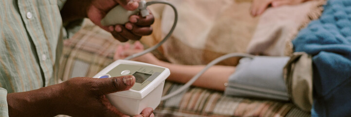 Senior Black man measuring blood pressure of senior Caucasian woman lying on bed, using digital...