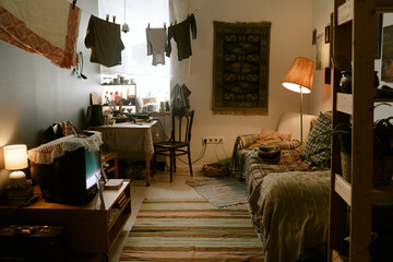 Cozy living room interior featuring sofa, television, desk with chair, hanging laundry and various household items arranged throughout small space, no people visible in scene