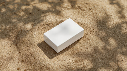 White rectangular box resting on textured sand with dappled sunlight white box