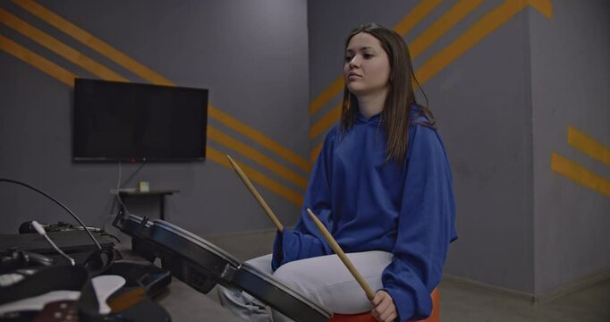 Young woman playing electronic drums in a modern studio. She is focused, passionate, and enjoying the music.