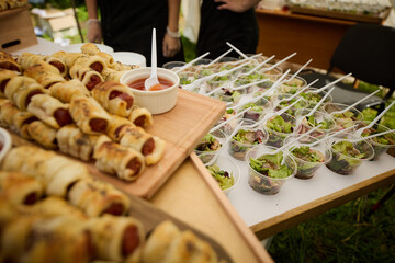 Appetizers of sausages in dough with tomato sauce and salad lie on a wooden board during a banquet