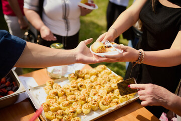 Hands of people taking food from a plastic plate during a banquet