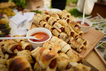 Appetizers of sausages in dough with tomato sauce and salad lie on a wooden board during a banquet
