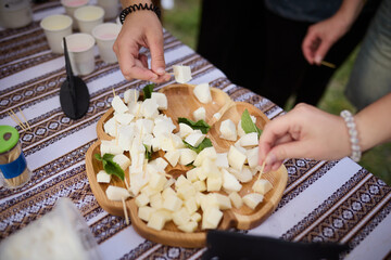 People take cheese cut into cubes from a wooden plate on a tablecloth with an ornament