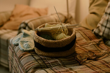 Knitting supplies resting on plaid sofa including yarn, knitting needles, finished knitted mittens...