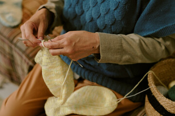 Senior Caucasian woman knitting with yarn, hands holding knitting needles while creating fabric,...
