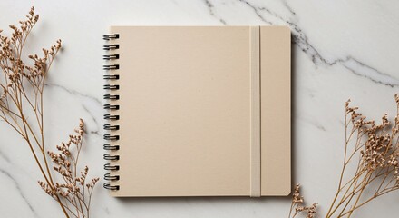Beige notebook with elastic band surrounded by dried flowers on marble background