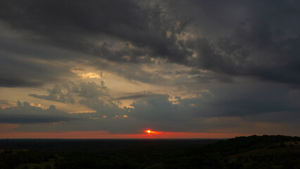 Evening rain clouds in the sky and sun on the horizon line at sunset.