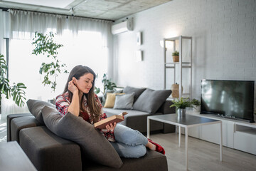 Obraz premium Young woman reading a book on the sofa in her living room