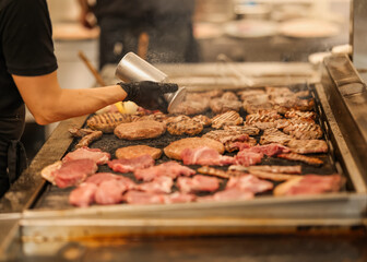 Chef seasoning various meats on a hot grill in a commercial kitchen. Fresh cuts sizzling as spices...