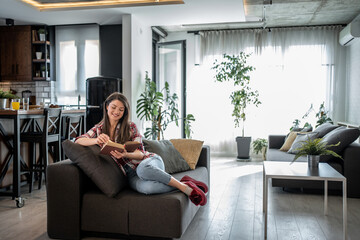 Young woman reading a book at home in modern living room