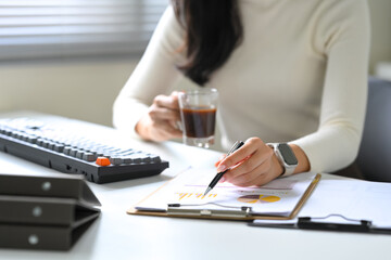 Close up of a businesswoman analyzing financial charts while enjoying a cup of coffee at her desk