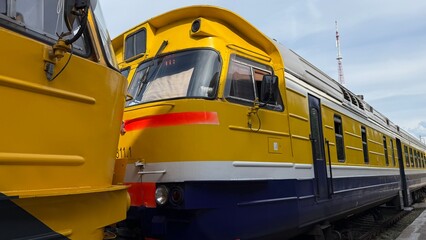Two colorful DR1A diesel trains parked on railway tracks at Daugavpils station, Latvia, on July 6, 2025. Yellow and orange-red locomotives represent Soviet-era railway engineering still in use today