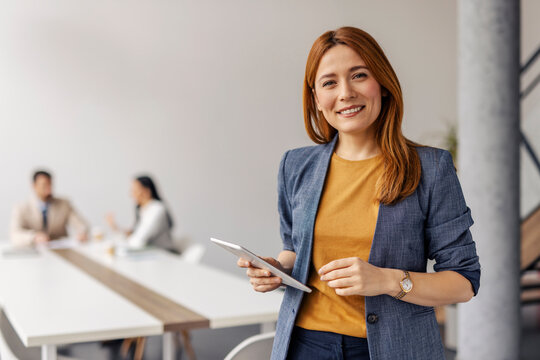 Portrait of happy businesswoman standing at corporate office during the meeting and smiling at camera.