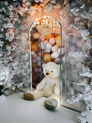 Cozy teddy bear sits in floral and balloon decorated corner with chandelier light