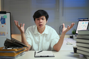 Tired businessman expressing stress and confusion during overtime hours in a cluttered office