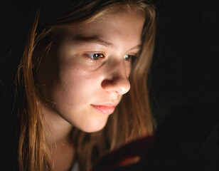 Teenager staring at phone in a dark room, face illuminated by screen light