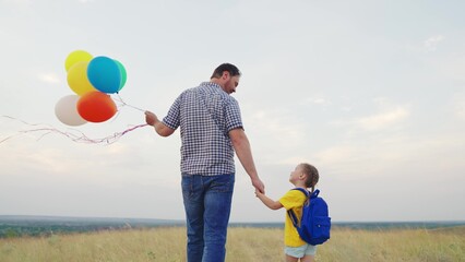 father holds small child with backpack by hand palm. happy family life. multi-colored balloons...