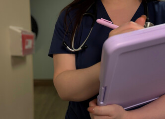 Nurse Writing on Clipboard in Hallway with Stethoscope Around Neck