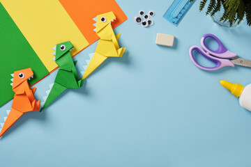 Origami work table with paper, googly eyes, scissors, glue bottle, ruler, and eraser on a light...