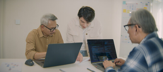 Asian senior software engineers working on laptops, discussing code and debugging in collaborative...