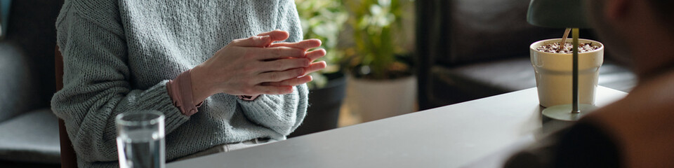Woman sitting at desk gesturing with hands during therapy session, facing unseen across table,...