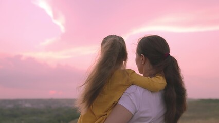 mom and daughter are hugging against the backdrop of pink sunset, a happy family, mom holds a child...