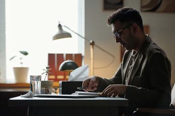 Man sitting at desk writing notes on clipboard during therapy session, eyeglasses and tissue box on...