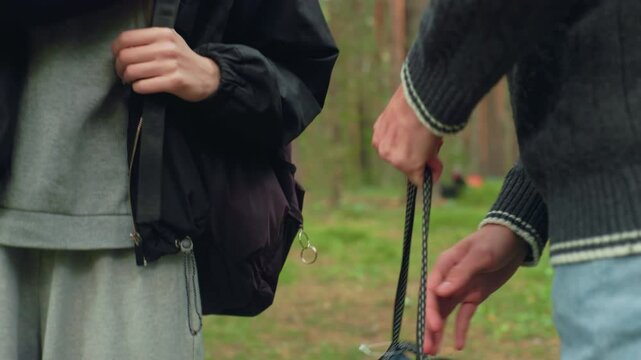 Close up of two companions halting during forest walk, hands relaxed near bags as they prepare to rest or nap, dressed in casual outdoor wear with natural woodland environment in background