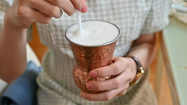 Woman using straw for stirring Lassi before drinking. Lassi is a traditional Indian drink made by blending yogurt with water and often flavored with spices, salt, sugar, or fruit.
