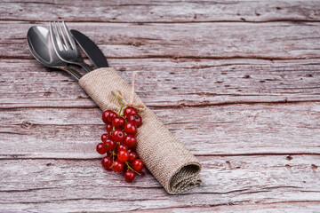 Rustic table setting with cutlery and red currants on wooden background