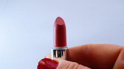 A woman's hand with red manicure twists red lipstick. Concept of facial care, makeup routine, and...