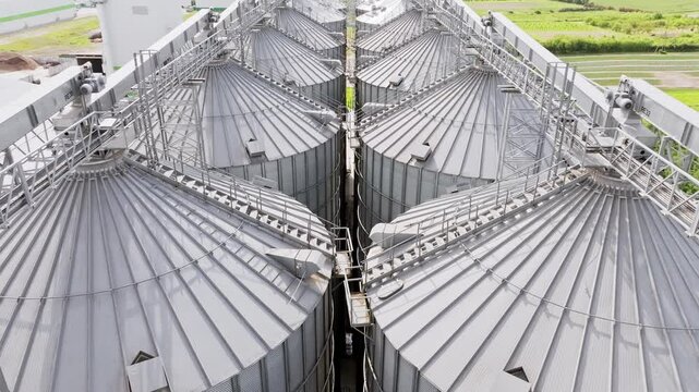 Smooth low drone flight moves forward above shiny silver grain silos in Latvia