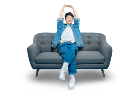 A contented young man in a denim jacket stretches his arms while sitting on a sofa, enjoying a relaxing break ON PNG 