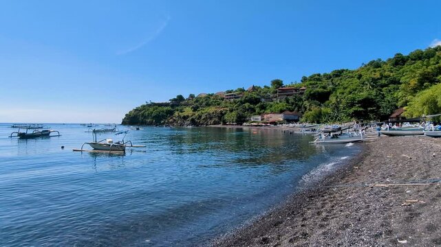 Scenic coastal landscape of black sand beach, fishing boats, and ocean in Amed on tropical island of Bali Indonesia