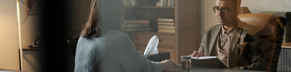 Man sitting at desk holding clipboard engaging in therapy session with woman sitting across table...