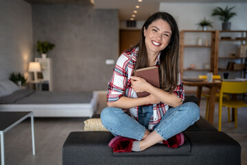Obraz premium Happy woman hugging a book while relaxing on sofa at home