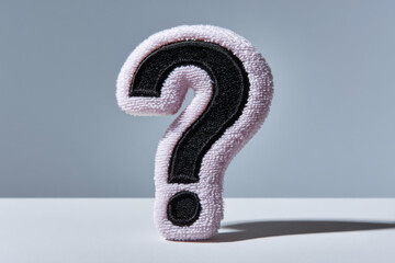 Pink fluffy question mark standing on white surface with gray background