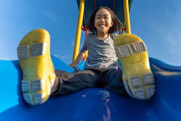 A little Asian girl playing at playground slide looking directly at the camera with a wide, joyful smile. Childhood play, fun, and excitement concept.