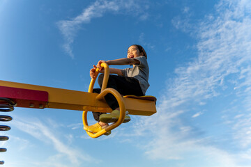 A happy young Asian girl on a yellow seesaw at a playground. Happiness, freedom, childhood fun, and...