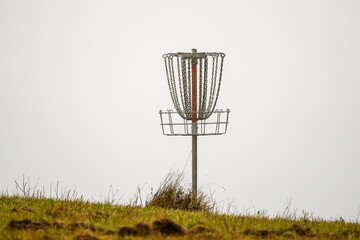 Frisbee golf basket (disc golf) silhouette on grass field hill top with grey sky background
