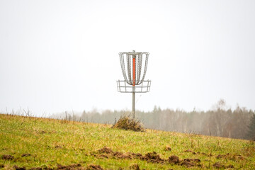 Close up of disk golf basket (Frisbee golf) on grass field hill with forest in the background on a...