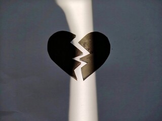 Minimalist black broken heart divided by a beam of light on dark background, symbolizing loss,...