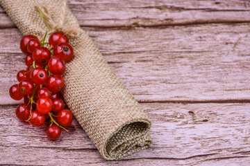 Close-up of fresh redcurrants on a wooden surface wrapped in burlap. Bright summer concept with...