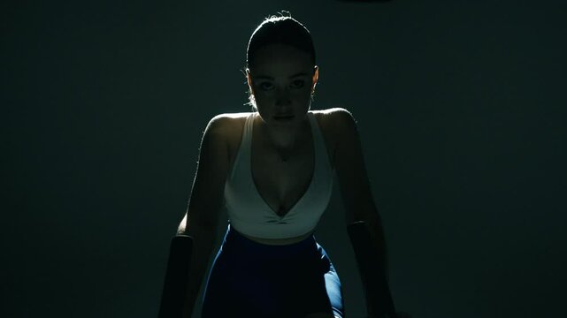 Atrakcyjna kobieta trenująca na rowerze stacjonarnym na siłowni w oswietleniem filmowym 